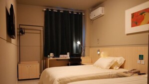 Una camera d'albergo con due letti, una scrivania, una sedia, una macchina del caffè, un condizionatore d'aria e un quadro appeso al muro.