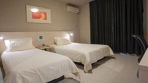 Camera d'albergo con due letti, un comodino, una scrivania, un condizionatore d'aria e un'ampia finestra con tende.