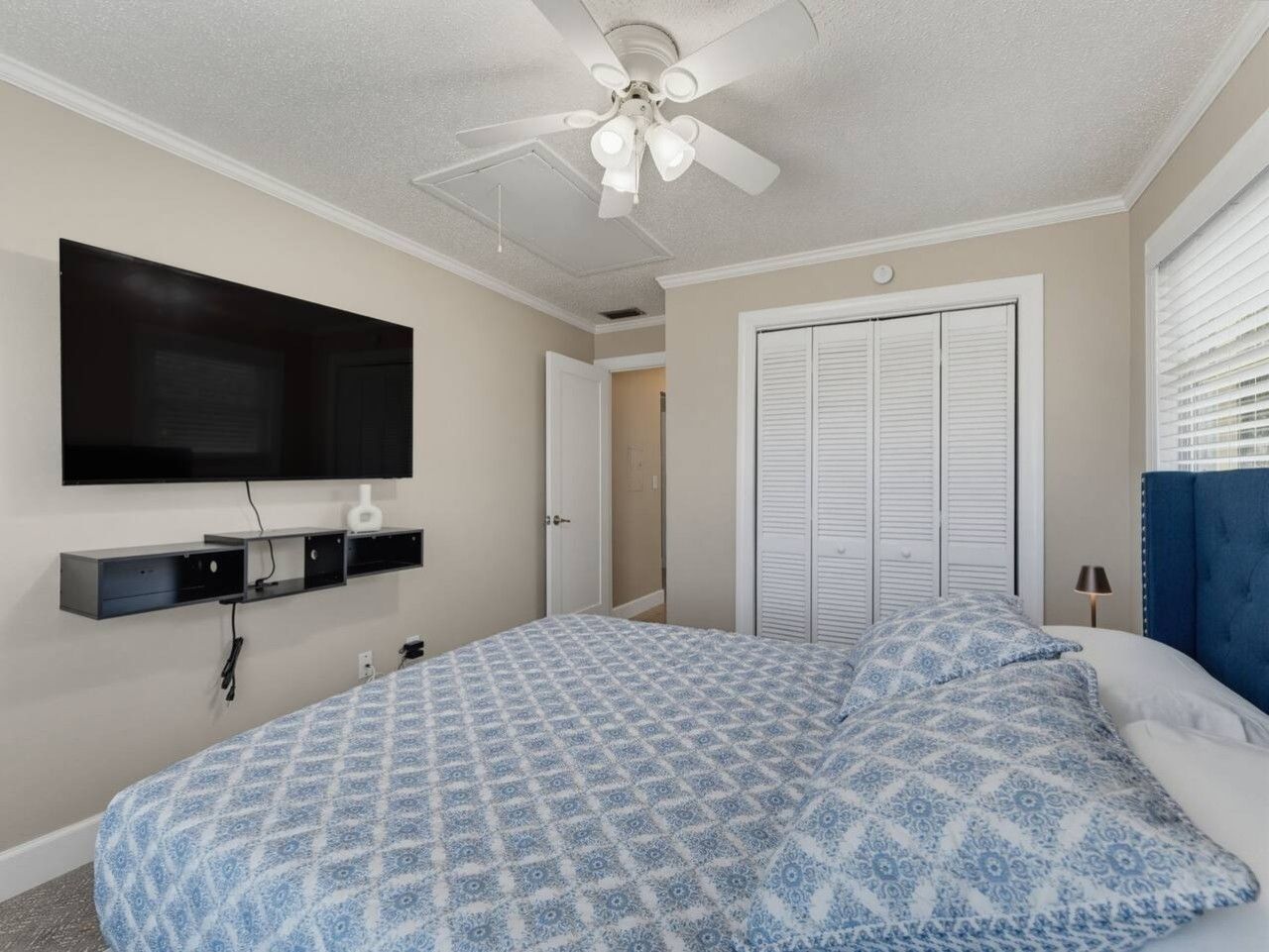 A bedroom with a bed, a ceiling fan, a TV mounted on the wall, and a closet with sliding doors.