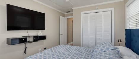 A bedroom with a bed, a ceiling fan, a TV mounted on the wall, and a closet with sliding doors.