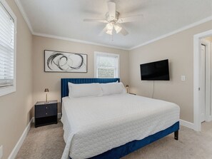 A bedroom with a bed, a ceiling fan, a wall-mounted TV, and a window with blinds. - Saltwater & Bubbles 5 | Indian Rocks Beach (Indian Rocks Beach)