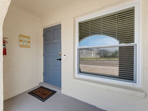 Eine blaue Tür mit Fußmatte, ein Fenster mit Jalousien und ein Schild an der Wand.