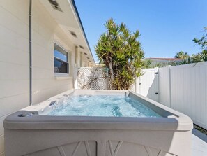Ein Whirlpool in einem Garten mit weißem Zaun und Palmen.
