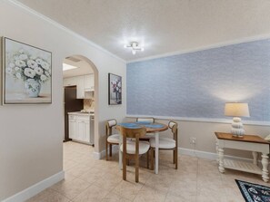 A dining area with a round table and chairs, a kitchen in the background, and a wall with a textured pattern. - Saltwater & Bubbles 4 | Indian Rocks Beach (Indian Rocks Beach)