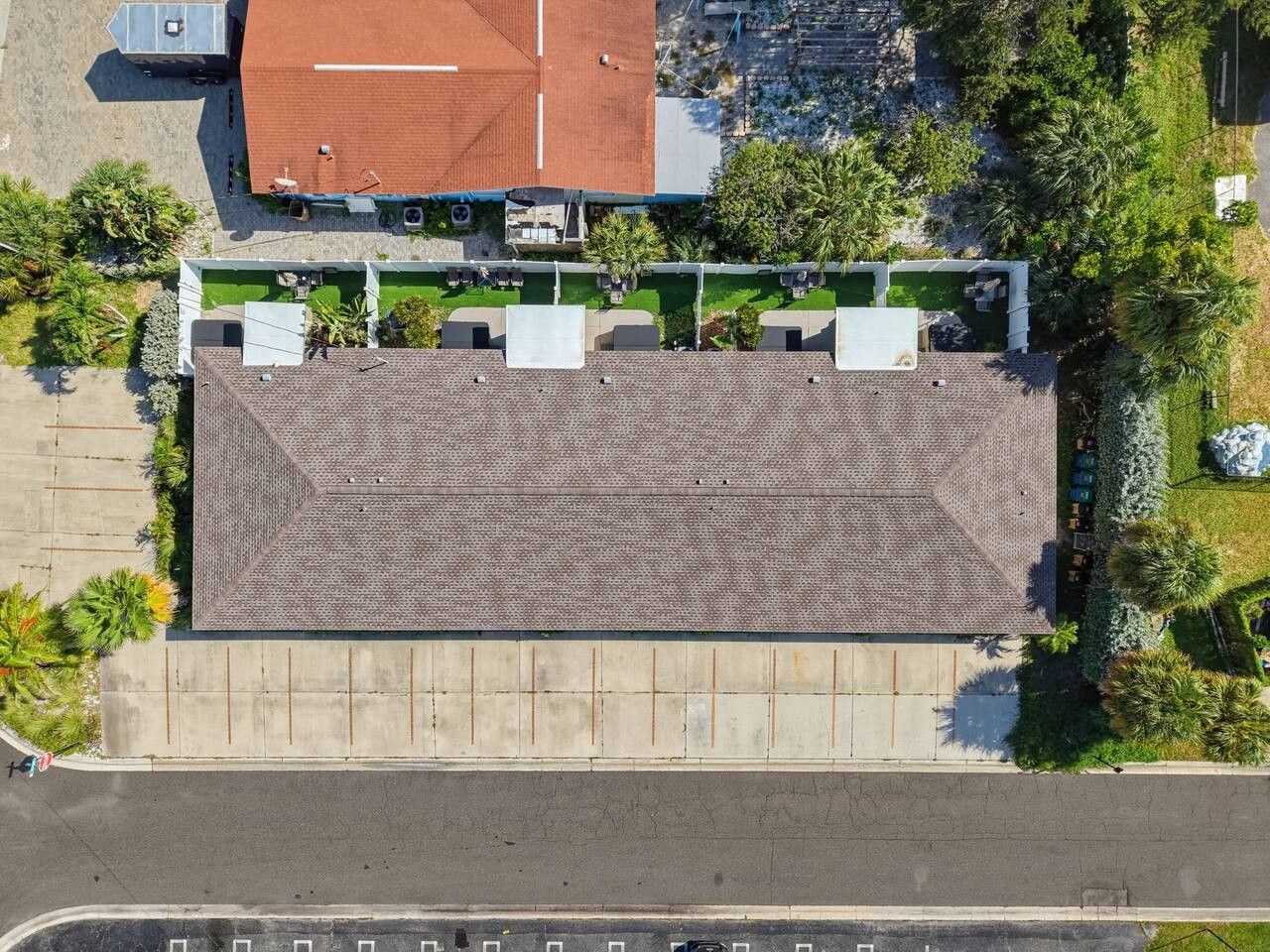 An aerial view of a building with a flat roof, surrounded by greenery and a parking lot.