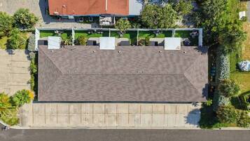 An aerial view of a building with a flat roof, surrounded by greenery and a parking lot.