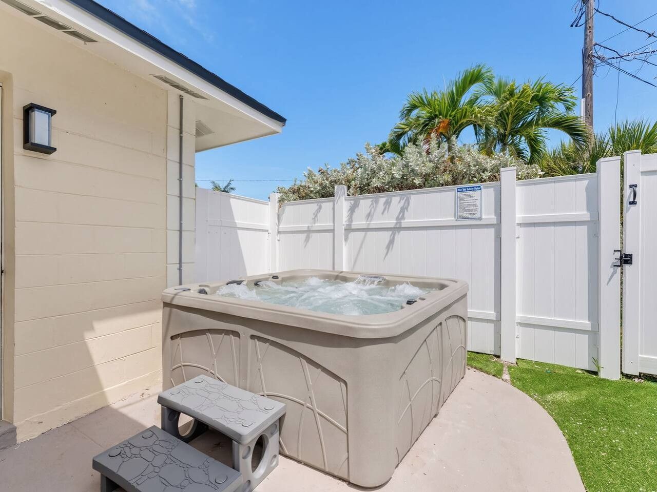 A hot tub in a backyard with a white fence, a small step leading to it, and a house in the background.
