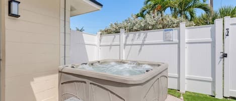 A hot tub in a backyard with a white fence, a small step leading to it, and a house in the background.