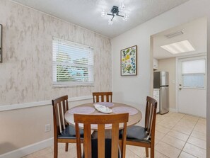 A dining area with a round table and four chairs, a window with blinds, a refrigerator, and a door with a window. - Saltwater & Bubbles 1 | Indian Rocks Beach (Indian Rocks Beach)