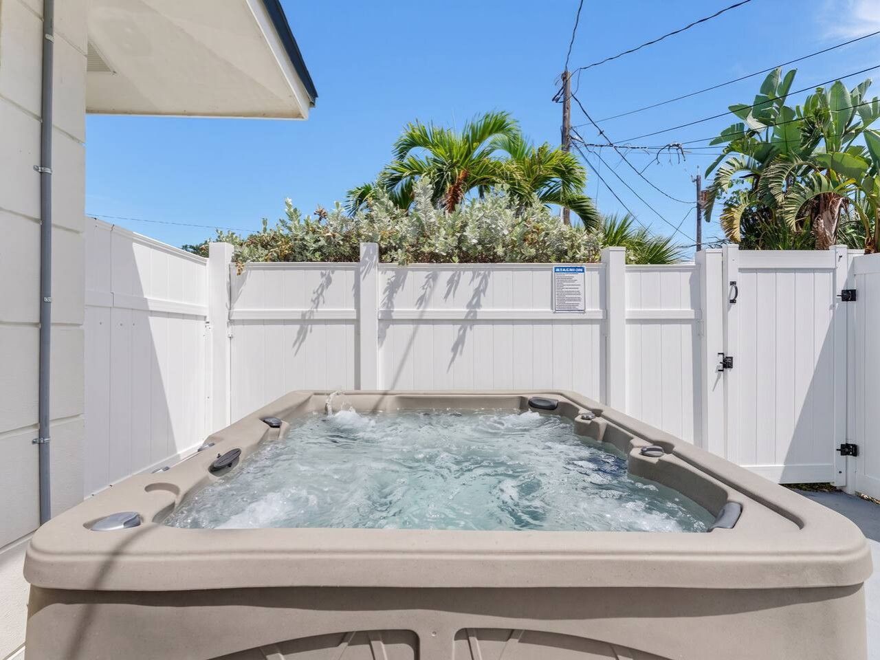 A hot tub with a white fence and palm trees in the background.