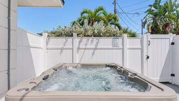 A hot tub with a white fence and palm trees in the background.