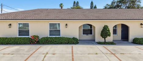 A single-story building with a flat roof, a front parking area, and a small tree in the center.