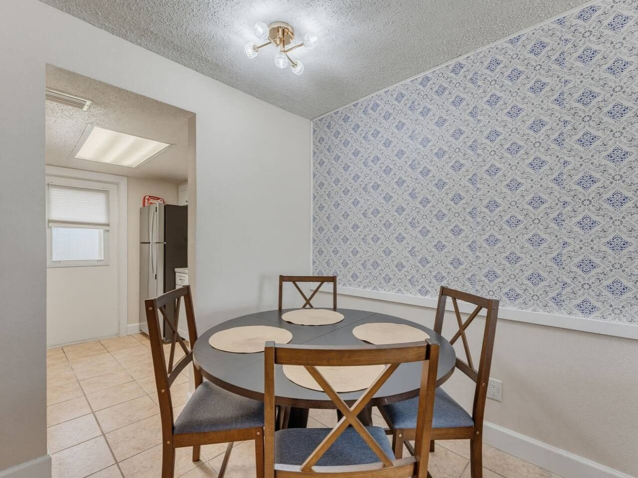 A dining area with a round table and four chairs, a ceiling light fixture, and patterned wallpaper.