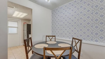 A dining area with a round table and four chairs, a ceiling light fixture, and patterned wallpaper.