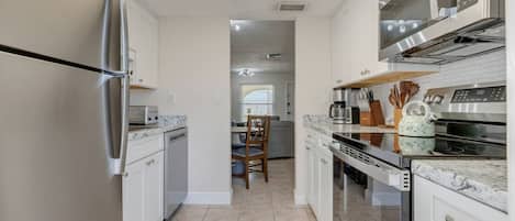 Een moderne keuken met witte kasten, roestvrijstalen apparatuur en een betegelde vloer.