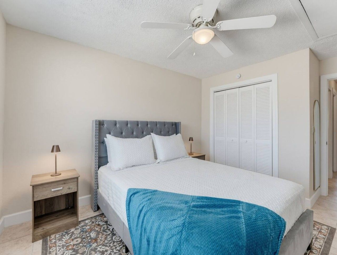 A bedroom with a bed, nightstands, a ceiling fan, a wardrobe, and a patterned rug.