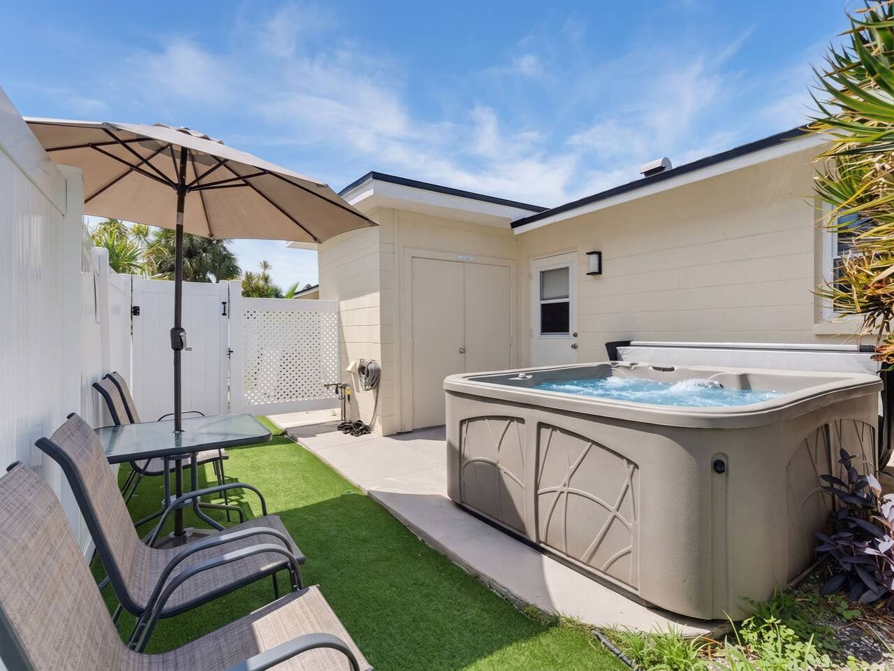 A backyard with a hot tub, a table with chairs, and a covered patio area.