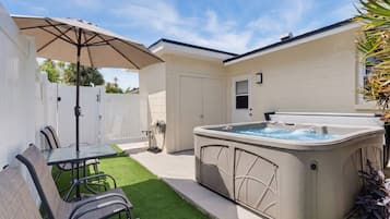 A backyard with a hot tub, a table with chairs, and a covered patio area.