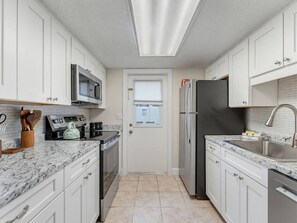 A kitchen with white cabinets, a stainless steel refrigerator, a microwave, and a sink. - Saltwater & Bubbles 2 | Indian Rocks Beach (Indian Rocks Beach)