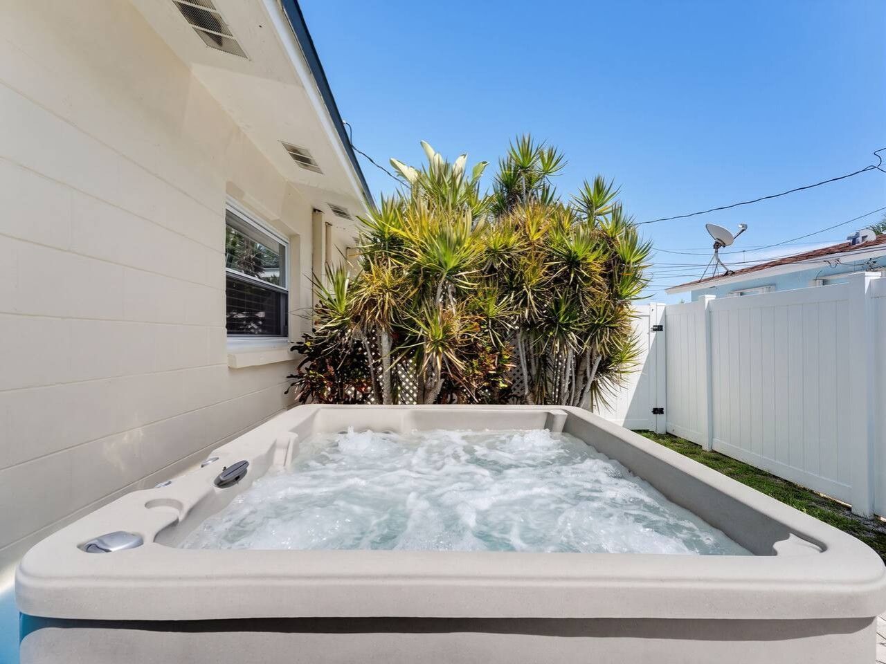 Un jacuzzi dans un jardin, avec une clôture blanche et des plantes tropicales.