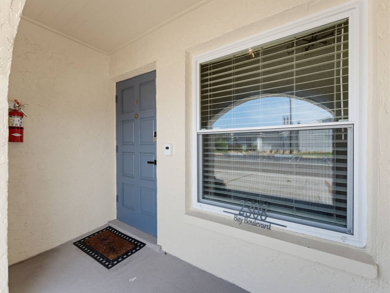 A blue door, a window with blinds, and a fire extinguisher on the wall.