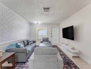 A living room with a sofa, armchairs, a coffee table, a TV, and a patterned rug. - Saltwater & Bubbles 2 | Indian Rocks Beach (Indian Rocks Beach)