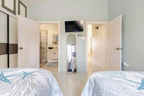Une chambre d’hôtel avec deux lits, une télévision et une salle de bain avec douche, ainsi qu’un couloir menant à une autre chambre.