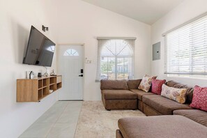 Un salon comprenant un canapé d’angle, un téléviseur fixé au mur et une porte avec une fenêtre.