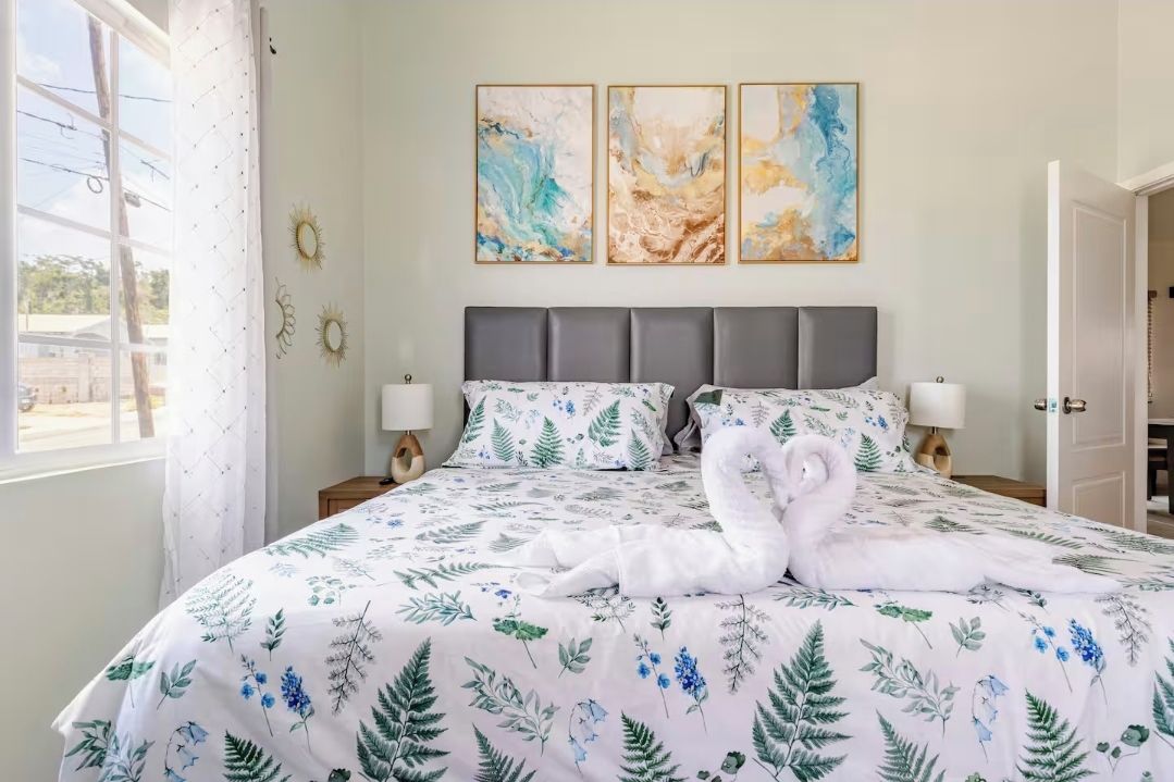 A bed with a floral bedspread, two wall-mounted paintings, and a window with curtains.