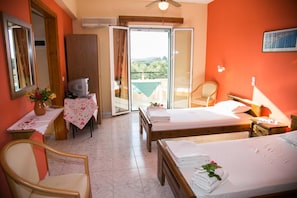 Ett hotellrum med två sängar, ett skrivbord med en dator, en stol, ett bord med en vas med blommor och en balkong med utsikt.
