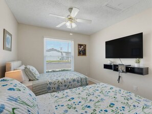 Ein Schlafzimmer mit zwei Betten, einem Deckenventilator, einem an der Wand montierten Fernseher und einem Fenster mit Jalousien.