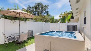 Ein Whirlpool mit weißer Außenverkleidung, umgeben von einer Terrasse mit Tisch und Stühlen sowie einem weißen Zaun.