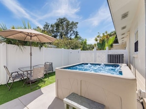 Ein Whirlpool mit weißer Außenverkleidung, umgeben von einer Terrasse mit Tisch und Stühlen sowie einem weißen Zaun.