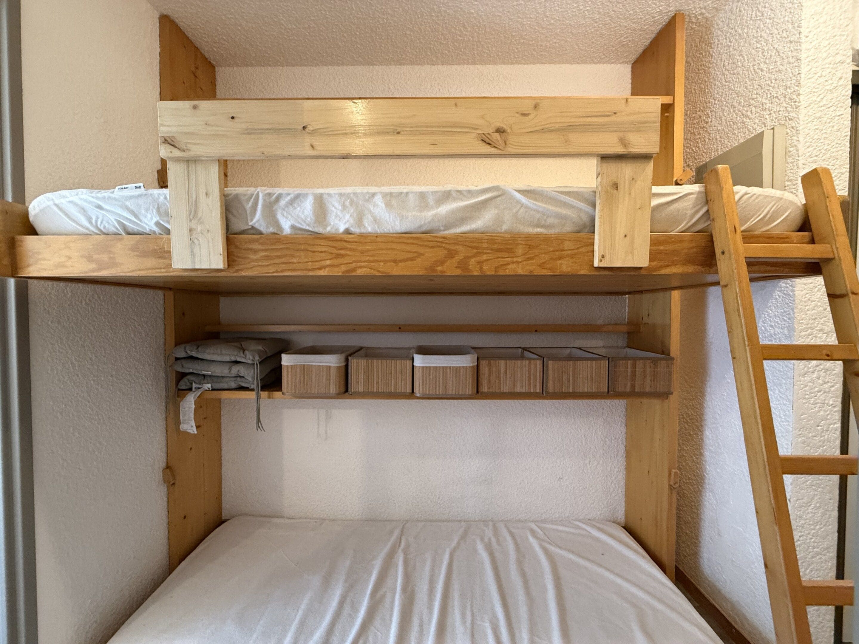 Una litera con estructura de madera, un estante inferior con cajas de almacenamiento y una escalera.