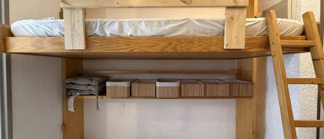 A bunk bed with a wooden frame, a lower shelf with storage boxes, and a ladder.