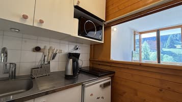 Una cocina con armarios blancos, un lavamanos de acero inoxidable y una ventana con vistas a árboles y edificios.