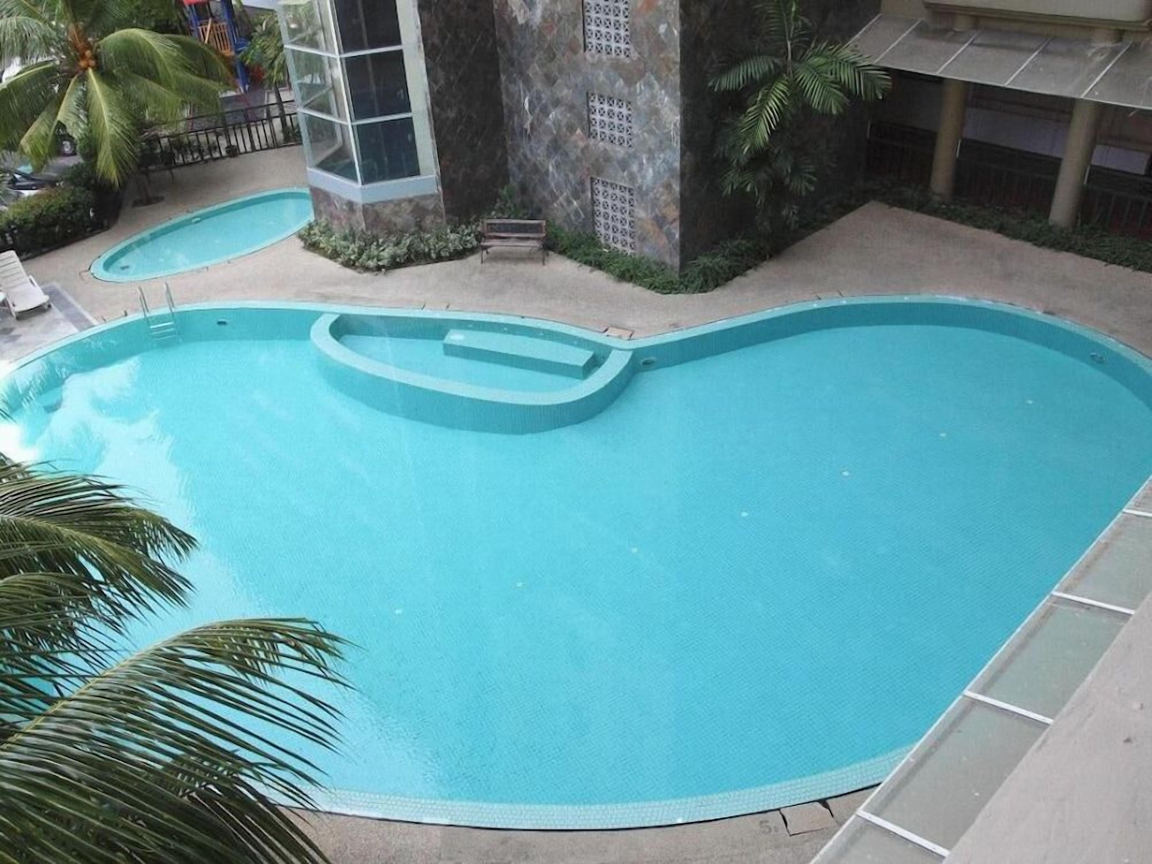 Une piscine au design incurvé, entourée de palmiers et d’un mur de pierre.