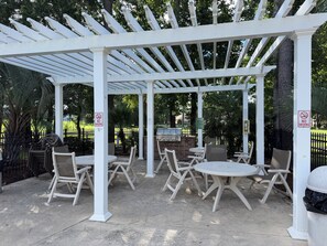 Eine überdachte Terrasse im Freien mit weißen Säulen und Tischen, inklusive Grill und Stühlen.