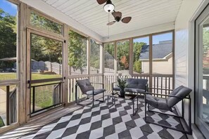 Eine überdachte Veranda mit Schachbrettmuster-Boden, zwei Stühlen, einem Tisch und einem Deckenventilator.