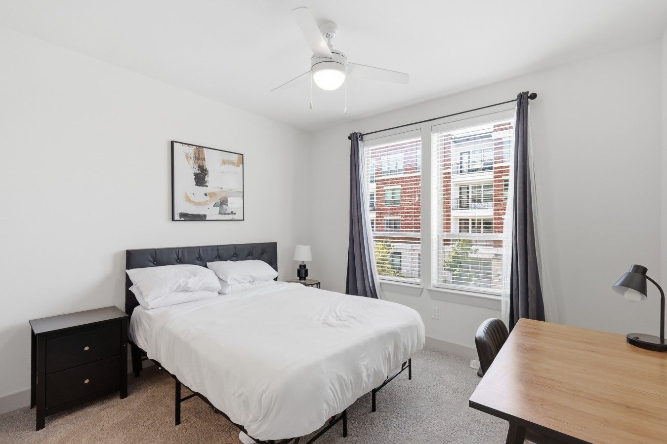 A bedroom with a bed, bedside tables, a desk, a ceiling fan, and a window with blinds.