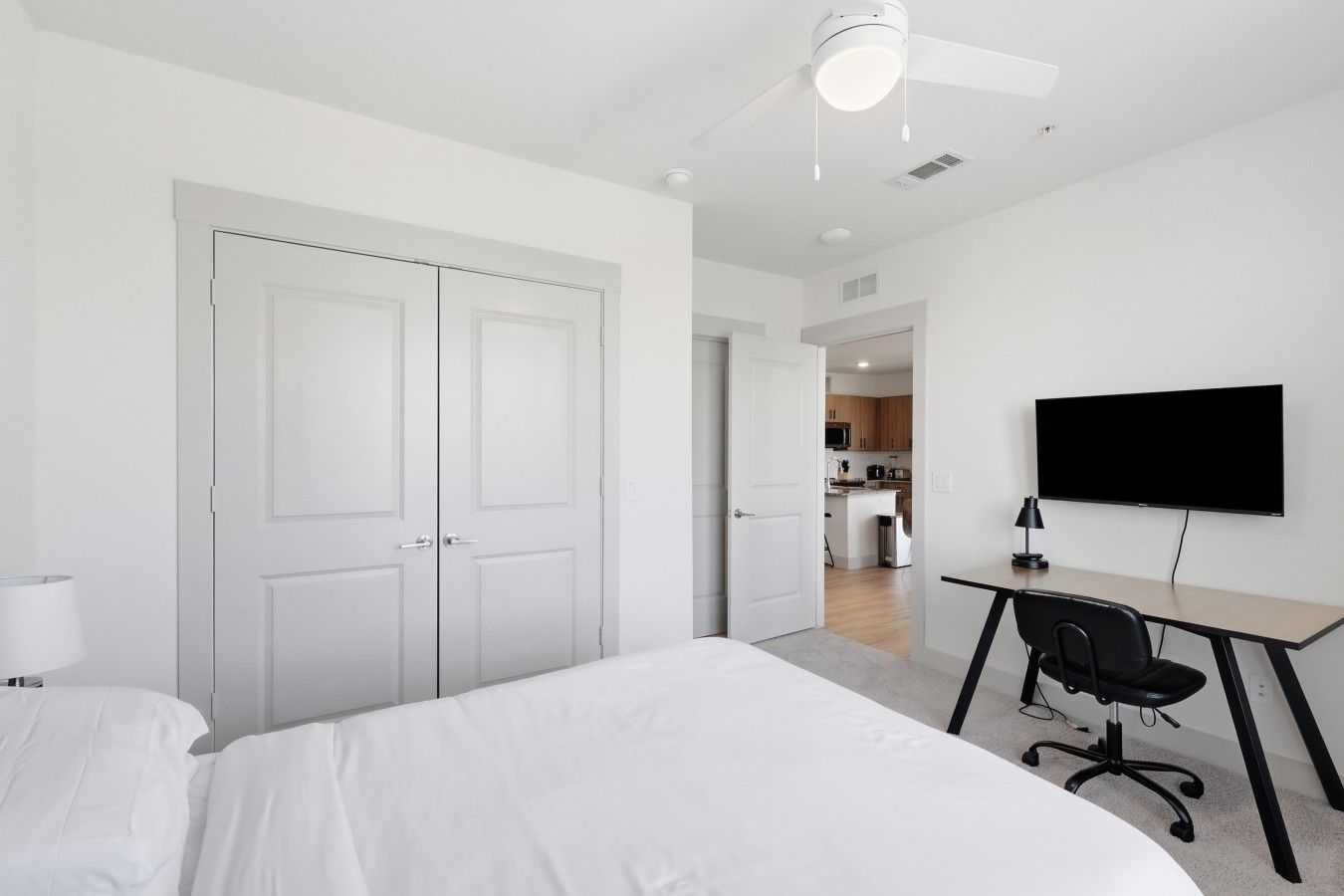 Quarto com cama, escrivaninha, cadeira, televisão e ventilador de teto.