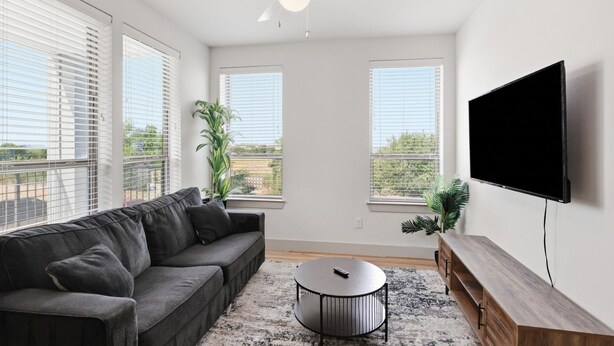 Uma sala de estar com sofá, mesa de centro, TV e ventilador de teto.