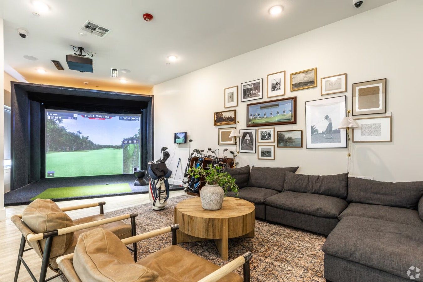 Un soggiorno moderno con un grande schermo che mostra una partita di golf, un divano, poltrone e un tavolino da caffè.