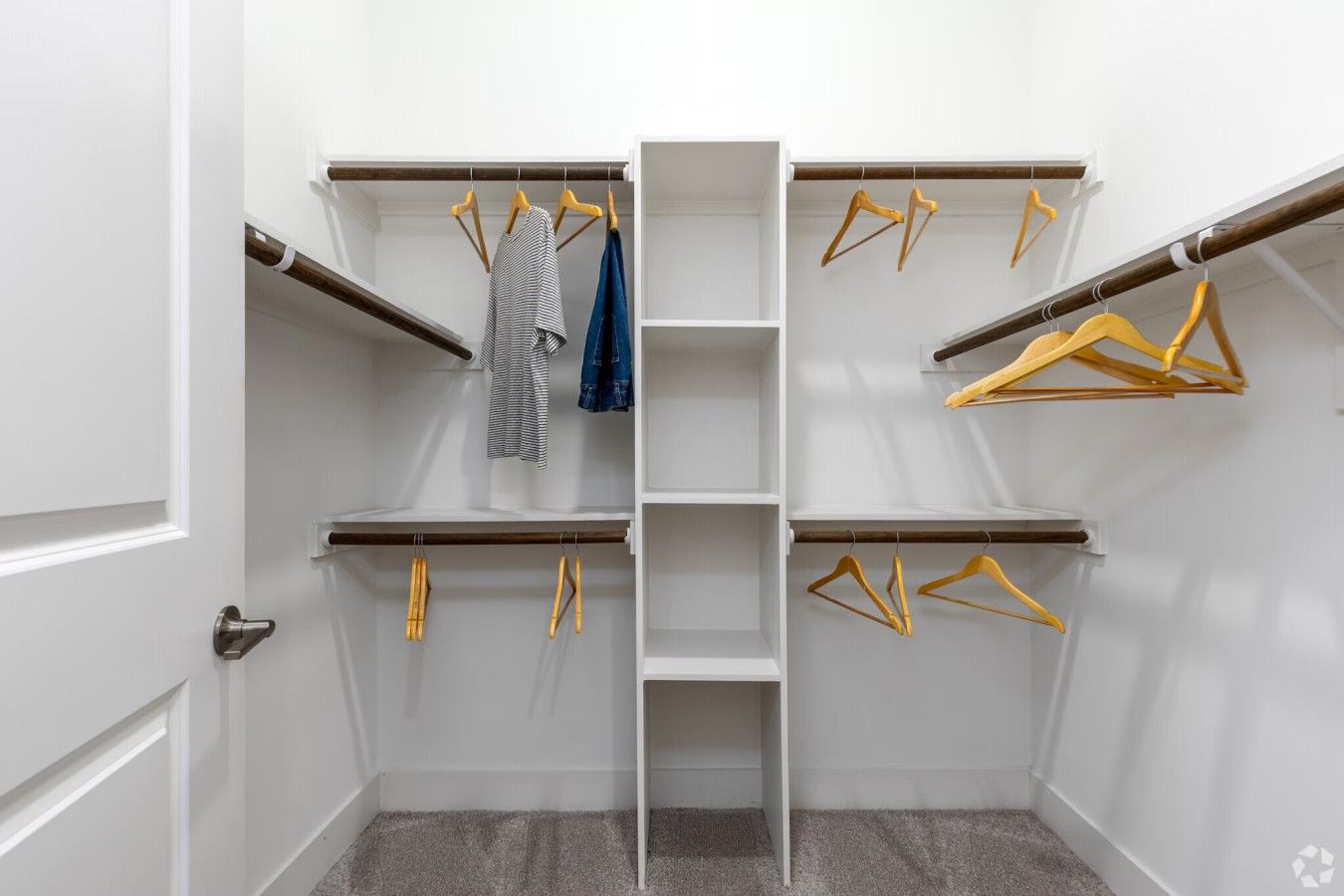 Un dressing avec de nombreuses étagères et un espace pour suspendre les vêtements, comprenant des cintres en bois et quelques vêtements.