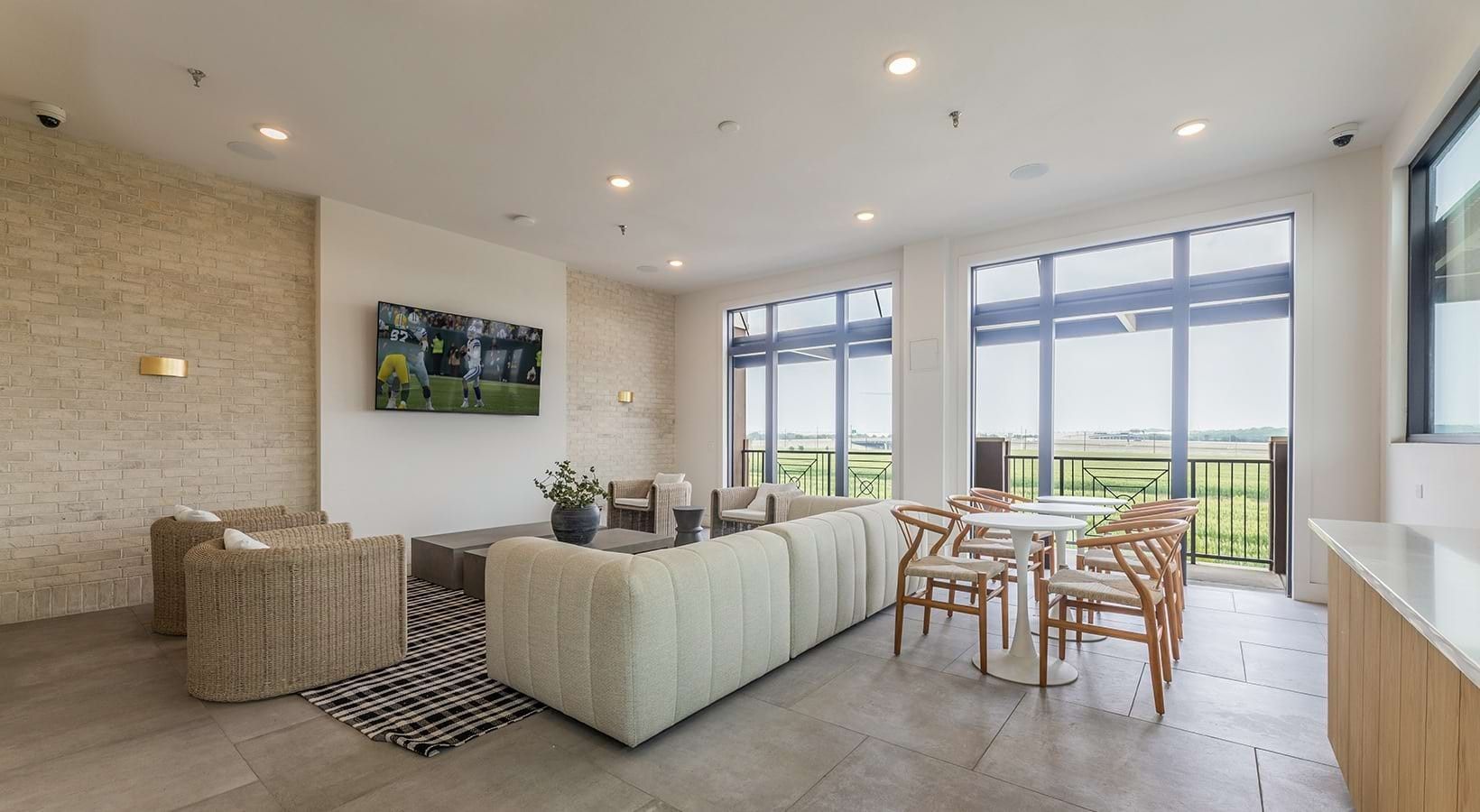 Una sala moderna con un sofá modular, un comedor con una mesa redonda y sillas, y ventanas amplias que ofrecen vistas al exterior.