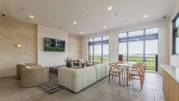 Una sala moderna con un sofá modular, un comedor con una mesa redonda y sillas, y ventanas amplias que ofrecen vistas al exterior.