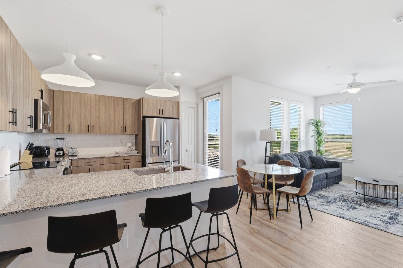 Una cucina moderna con isola centrale, zona pranzo con sedie e angolo living con divano e tavolino.