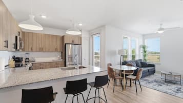 Una cucina moderna con isola centrale, zona pranzo con sedie e angolo living con divano e tavolino.