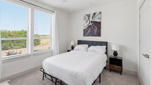 Quarto com cama, mesas de cabeceira, ventoinha no teto e janela com persianas.