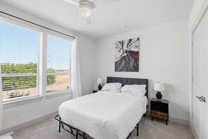 Een slaapkamer met een bed, nachtkastjes, een plafondventilator en een raam met zonwering.